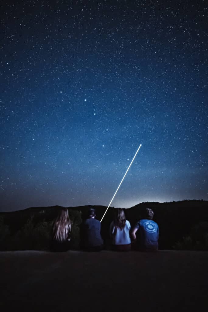 Four people gazing at a starry night sky, with a bright light streaking across.